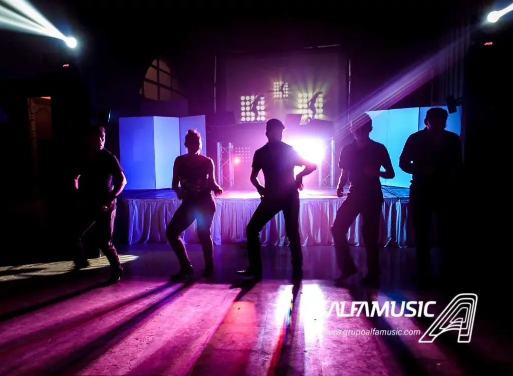 Escenario de Dj Alfamusic con luces de colores, al frente se ven las siluetas de cuatro animadores bailando
