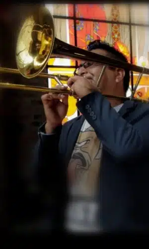 Rafael Bautista, Trombonista, tocando su instrumento con un bello vitral al fondo, durante una presentación del grupo versátil Alfamusic