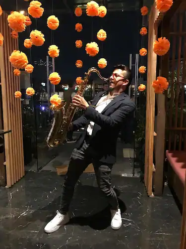 Muro Saxofonista tocando música en un evento con flores naranjas y decoración de madera.